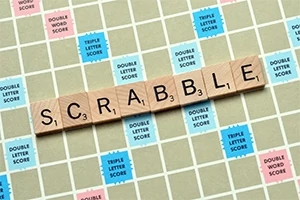木製のタイルで「SCRABBLE」と綴り、カラフルなポイントマスのあるゲームボードの上に置かれている。