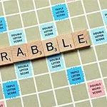 木製のタイルで「SCRABBLE」と綴り、カラフルなポイントマスのあるゲームボードの上に置かれている。